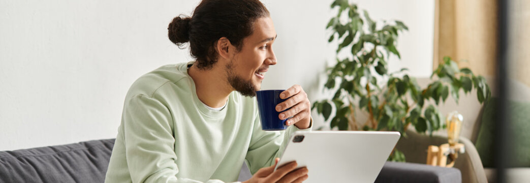 Young man enjoying coffee while using a tablet in a cozy home environment during morning hours