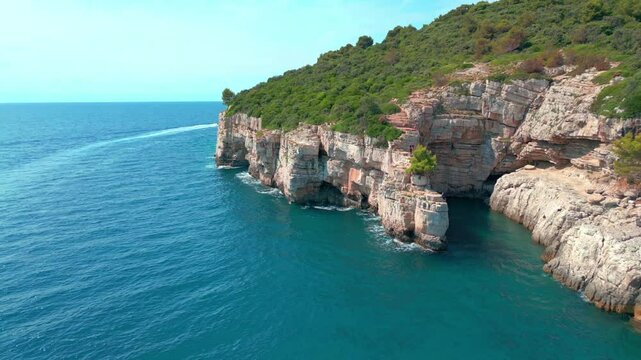Scenic view of a steep rocky coastline near Pula - Kanjon Muzil, covered in dense green vegetation, extending into the turquoise Adriatic Sea