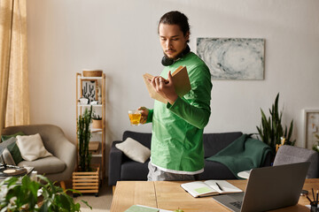 Young handsome man enjoying a quiet afternoon at home while reading and sipping a drink