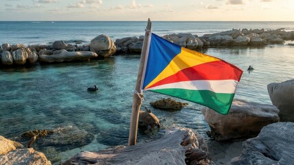 Flag Seychelles displayed on wooden pole at pristine rocky coastline with crystal clear turquoise waters and granite boulders