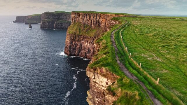 Flying over path near the edge of Cliff of Moher - one of the most popular tourist destinations in Ireland. Aerial breathtaking cliffs of Moher in Ireland, County Clare