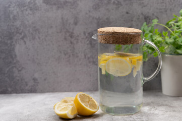 Refreshing lemon water in a glass jug on a concrete background, a glass jug filled with fresh lemon...