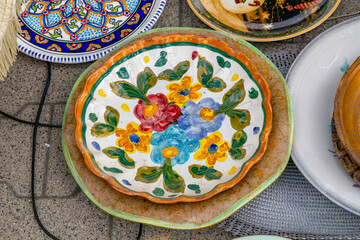 Colorful hand-painted plate with floral design displayed at a flea market. Decorative folk-style pottery.