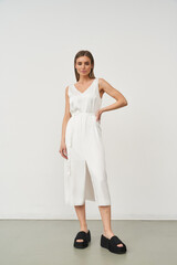 Woman in a sleeveless, knee-length white dress standing confidently with one hand on her hip,...