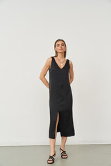 Elegant woman wearing a sleeveless, knee-length black dress with a V-neck and side slit, standing...
