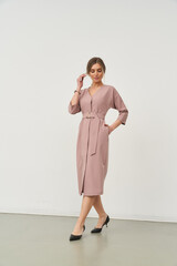 Fashionable woman in a pink belted knee-length dress and black heels stands confidently, posing...