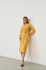 Elegant Caucasian woman in stylish yellow dress posing indoors in modern studio space