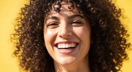 Fototapeta premium Smiling young hispanic female with curly hair against yellow background