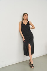 Elegant woman in a sleeveless black dress with a thigh-high slit, standing with one hand on hip,...