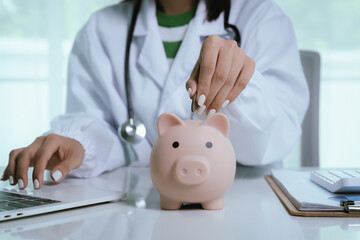 Close up young female general practitioner putting coin in piggy bank, managing hospital budget...
