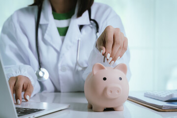 Close up young female general practitioner putting coin in piggy bank, managing hospital budget...