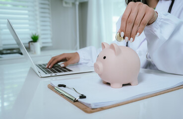 Close up young female general practitioner putting coin in piggy bank, managing hospital budget...