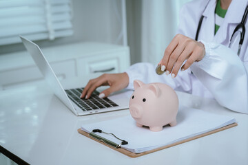 Close up young female general practitioner putting coin in piggy bank, managing hospital budget...