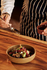 Chef pouring olive oil from ladle onto gourmet dish in wooden bowl. Atmospheric fine dining service...