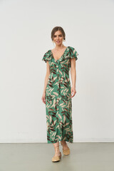 A woman smiles, wearing a green dress with a leaf pattern, featuring short ruffled sleeves and a...