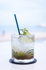 Refreshing cocktail with mint and lime served in a glass, perfect for summer relaxation by the beach.
