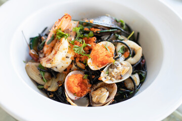 Squid ink spaghetti with garlic, olive oil, chili and seafood on white dish.