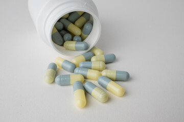 White bottle container with medication capsules on light grey background with copy space.