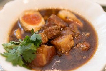 Delicious bowl of savory pork stew with eggs and fresh herbs garnishing.