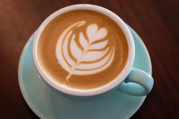 Cup of coffee with latte art on wooden table with soft sunlight. Top view