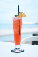 A refreshing tropical cocktail served in a tall glass, garnished with a slice of lemon and mint, perfect for beach settings.