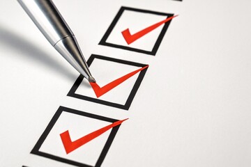 Silver pen marking red checkmarks on a white checklist paper