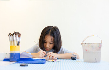Young Asian girl focuses on painting a clay object, with her hand and brush with selective focus shows creativity and calm concentration for kid learning activity  via art and development in child.