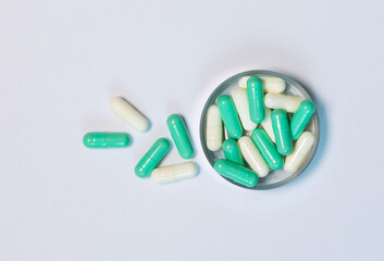 Close-up top-view of green and white capsule pills in a metal container on white background. Lay...