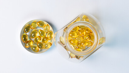 Close-up yellow fish oil capsules in a glass jar. Lay flat composition highlights supplements, softgel texture, and health care concept with clean white background for wellness and nutrition.