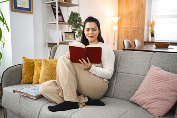 Woman reading a book while relaxing on a sofa at home