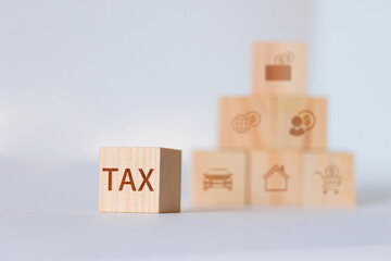 A wooden block with the word TAX is in focus, with a blurred pyramid of blocks showing various...