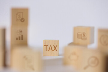 The TAX wooden block is in sharp focus, surrounded by blurred blocks with other financial icons,...