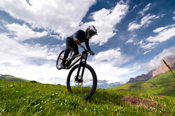 professional man in a full-face helmet performs a front wheelie trick in a field in the mountains...