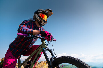 Portrait of a young man in a protective helmet and gloves, in bright clothes, sitting on a downhill...