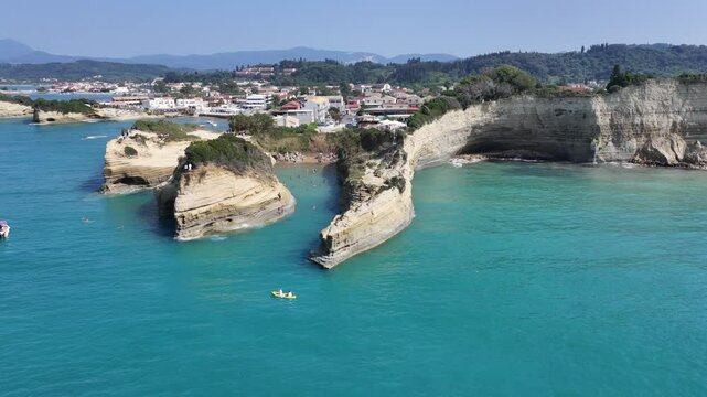 4k aerial video footage flying around sandstone cliffs of "Kanali tou Erota" beach at Sidari coastline in north part of Corfu Island with Sidari Cityscape in background