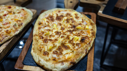 A freshly baked flatbread pizza topped with melted cheese and pineapple, served hot on a wooden...