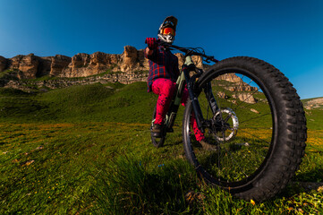 Wide angle shot of a downhill mountain bike wheel in the foreground, with the athlete sitting...
