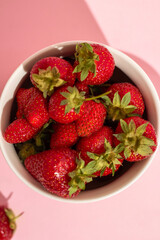 Fresh ripe delicious strawberries in a white bowl isolated on a pink background