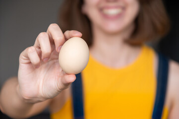woman's hand holds a raw chicken egg against the background of herself and her smile. Portrait of...