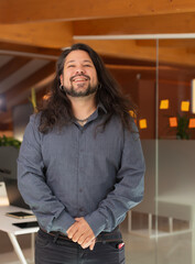 Portrait of a man with long hair, beard and earrings, smiling at the office in the office