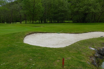 Greenkeeper is maintaining golf course with bunker and rake on sunny day