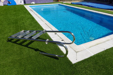Metal ladder lying on artificial turf by private swimming pool