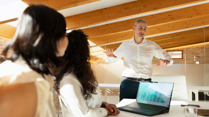 An adult man speaks and exposes his ideas to other colleagues who remain attentive, during an office meeting