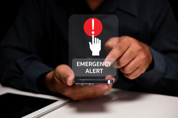 A person holding a smartphone with a digital emergency alert notification displayed above the...