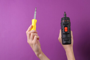 Female hands holding cordless screwdriver and screwdriver on purple background