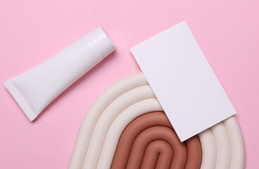 Geometric line podium with white cream tube and white business card on pink background. Creative...