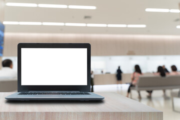 Laptop with blank screen on wooden table in bright waiting area lobby with people sitting and blurred background