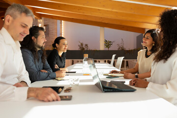 A group of people, women and men, discuss with good mood, during an office meeting