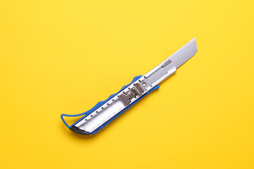 Obraz premium Metal stationery knife on a yellow background