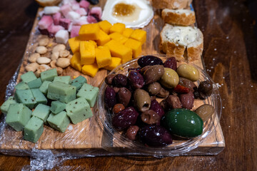 A rustic wooden cheese board with cubes of colorful cheese, a bowl of assorted olives, fresh bread,...